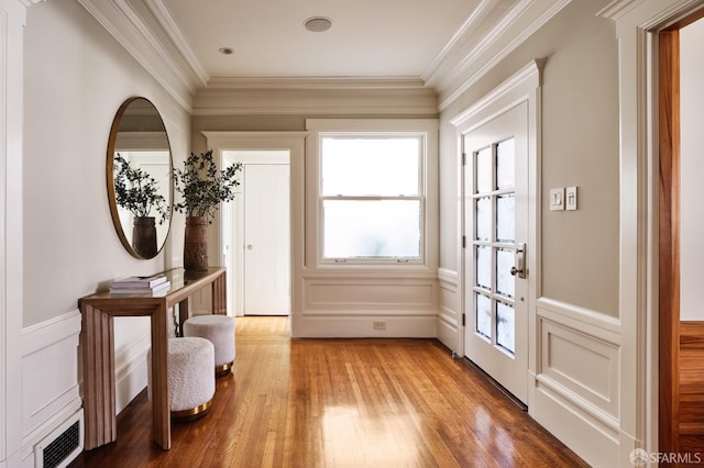 doorway to outside featuring a decorative wall, visible vents, crown molding, and light wood finished floors