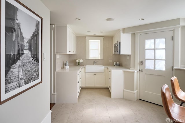 kitchen featuring tasteful backsplash, stainless steel microwave, light countertops, a sink, and white cabinetry