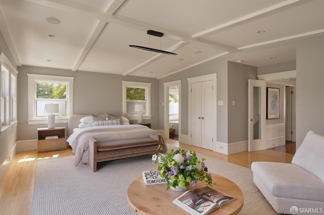 bedroom with light wood finished floors, vaulted ceiling with beams, and baseboards