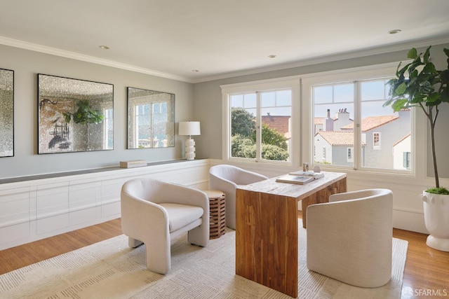 living area with light wood-style floors, a wainscoted wall, and ornamental molding