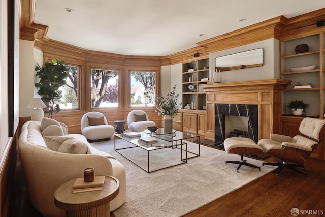 living room with ornamental molding, wood finished floors, built in features, and a premium fireplace