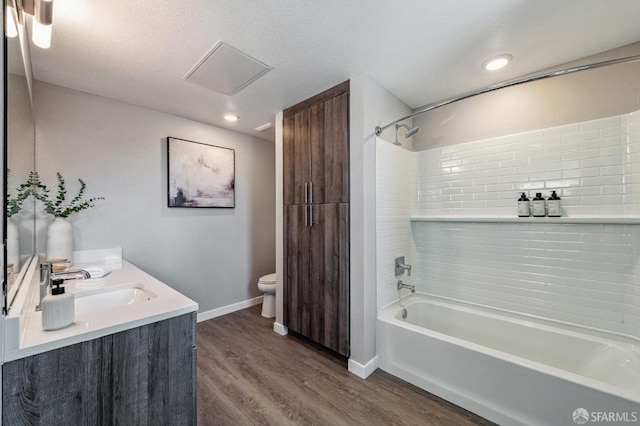 full bathroom with hardwood / wood-style flooring, vanity, tiled shower / bath combo, toilet, and a textured ceiling