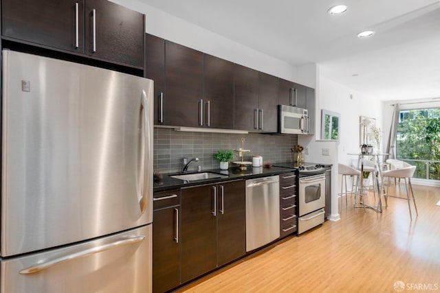 kitchen with appliances with stainless steel finishes, tasteful backsplash, dark brown cabinets, sink, and light hardwood / wood-style floors