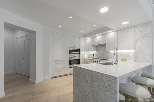 kitchen with sink, white cabinetry, backsplash, double oven, and light wood-type flooring