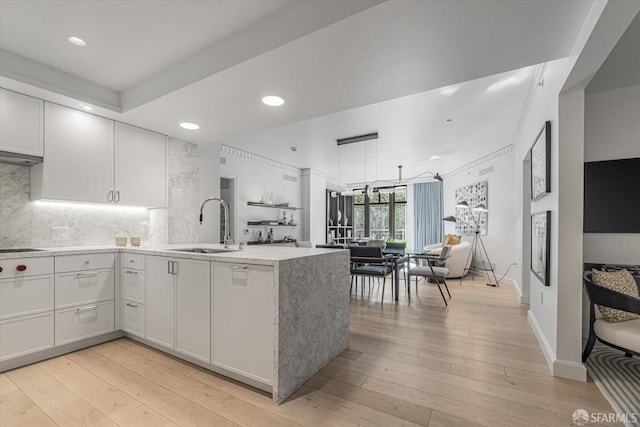 kitchen featuring white cabinetry, sink, decorative backsplash, kitchen peninsula, and light wood-type flooring