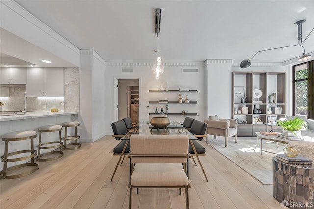 dining space featuring crown molding, sink, and light wood-type flooring