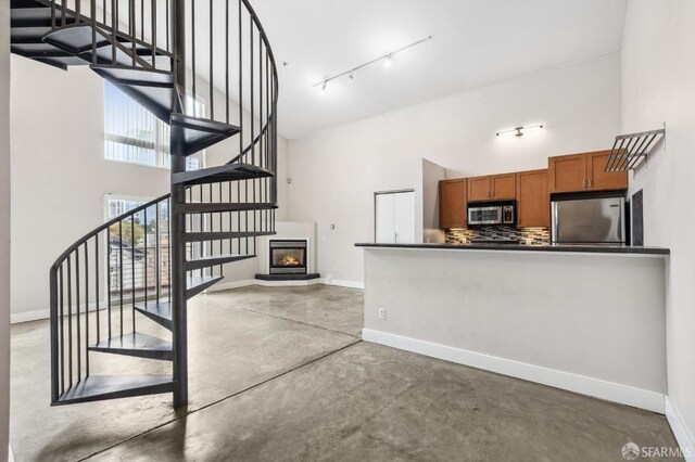 stairway featuring a towering ceiling, track lighting, and concrete flooring