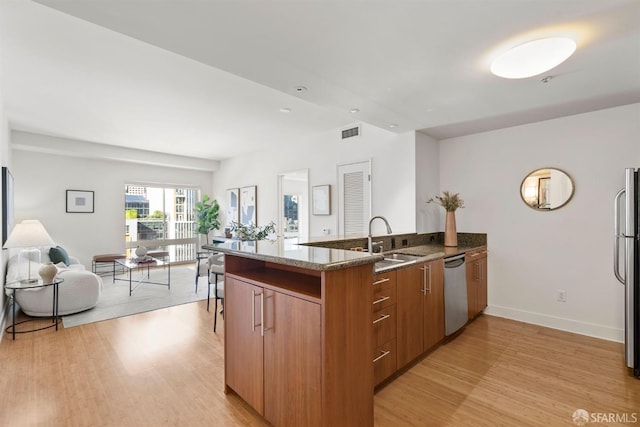 kitchen with sink, dark stone countertops, light hardwood / wood-style floors, kitchen peninsula, and stainless steel appliances