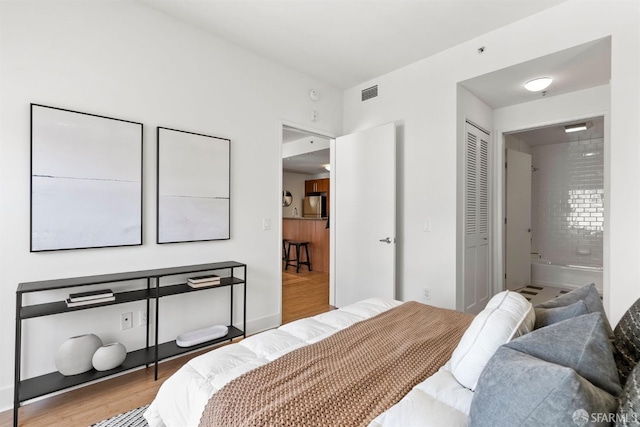 bedroom with ensuite bath, refrigerator, a closet, and light wood-type flooring