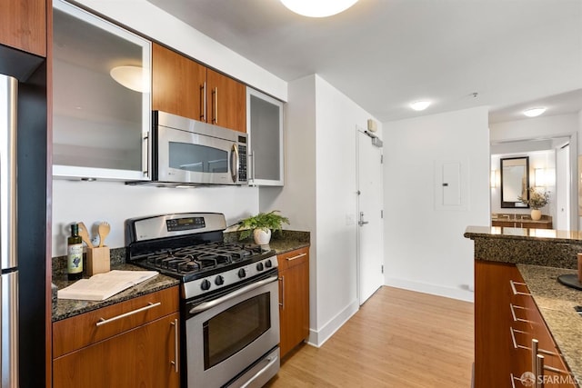 kitchen with stainless steel appliances, dark stone counters, and light wood-type flooring