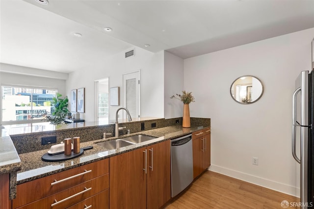 kitchen with appliances with stainless steel finishes, sink, dark stone countertops, and light wood-type flooring