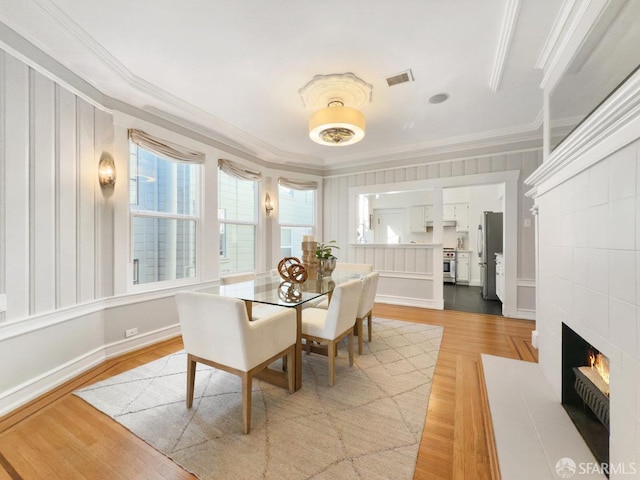 dining room featuring ornamental molding, a fireplace, and light hardwood / wood-style floors