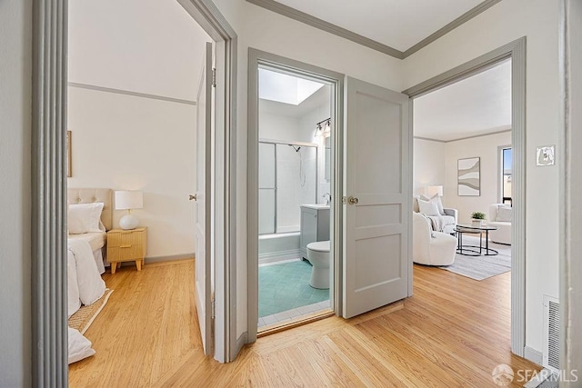 hallway with light wood-type flooring, baseboards, and ornamental molding