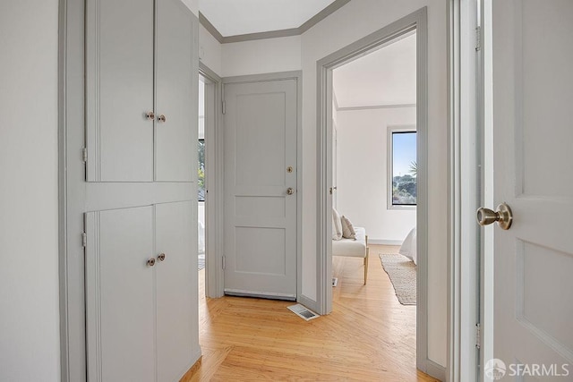 corridor with visible vents, baseboards, light wood-type flooring, and ornamental molding