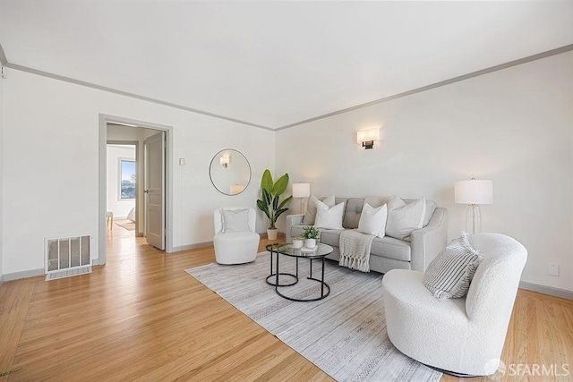 living area with visible vents, baseboards, crown molding, and light wood finished floors