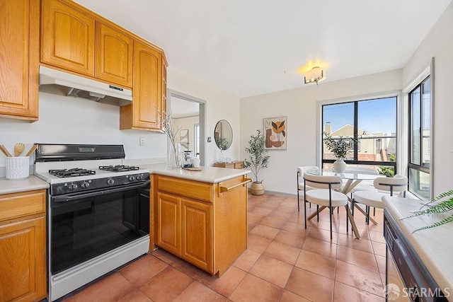 kitchen with under cabinet range hood, range with gas cooktop, a peninsula, light countertops, and light tile patterned floors