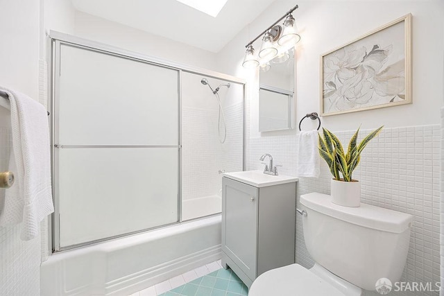 full bathroom with vanity, tile walls, toilet, and combined bath / shower with glass door