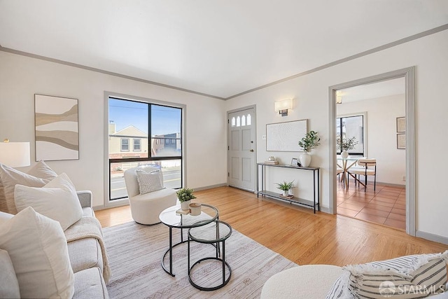 living area with baseboards, light wood-style flooring, and crown molding