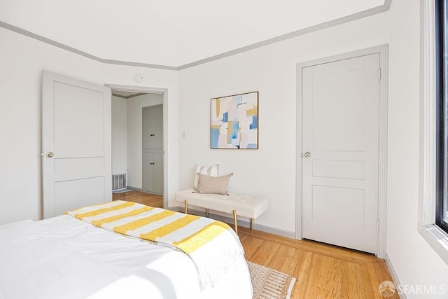 bedroom featuring light wood-style flooring, visible vents, baseboards, and ornamental molding