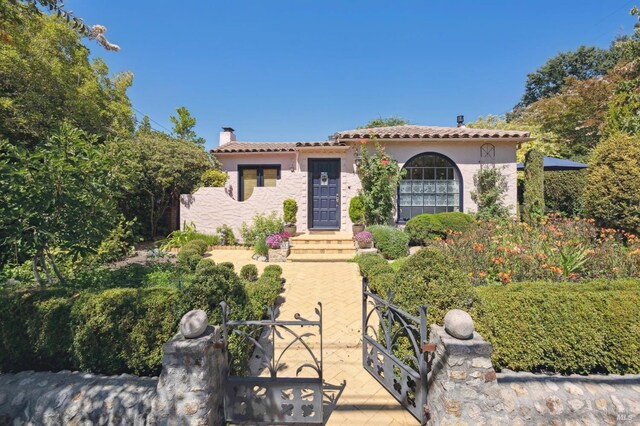 mediterranean / spanish-style house featuring a gate, a tile roof, a chimney, fence, and stucco siding