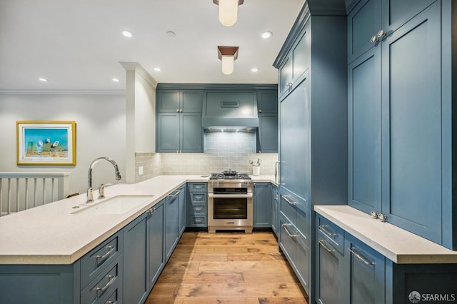 kitchen featuring stainless steel range, sink, kitchen peninsula, light hardwood / wood-style floors, and decorative backsplash