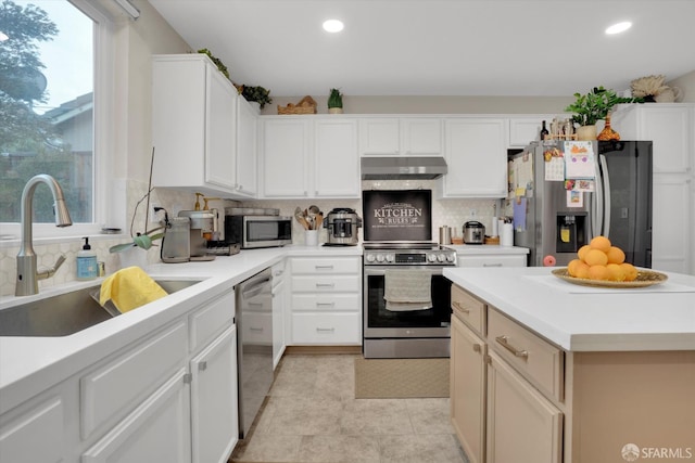 kitchen featuring under cabinet range hood, a sink, a healthy amount of sunlight, appliances with stainless steel finishes, and decorative backsplash