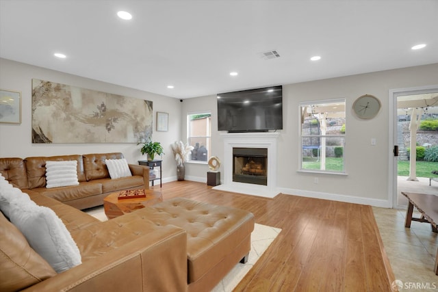 living room with light wood finished floors, baseboards, visible vents, a fireplace with raised hearth, and recessed lighting