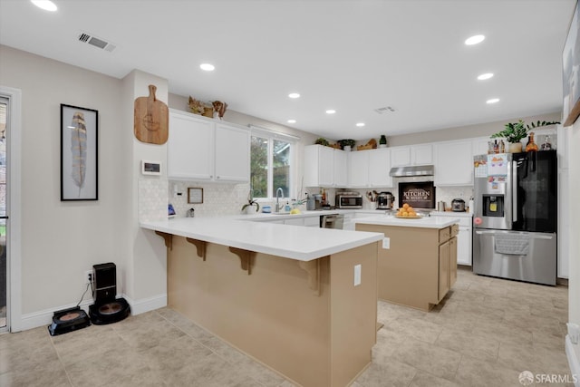 kitchen featuring visible vents, appliances with stainless steel finishes, a kitchen island, a peninsula, and under cabinet range hood