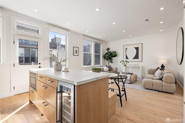 kitchen with a kitchen island, beverage cooler, and light hardwood / wood-style floors