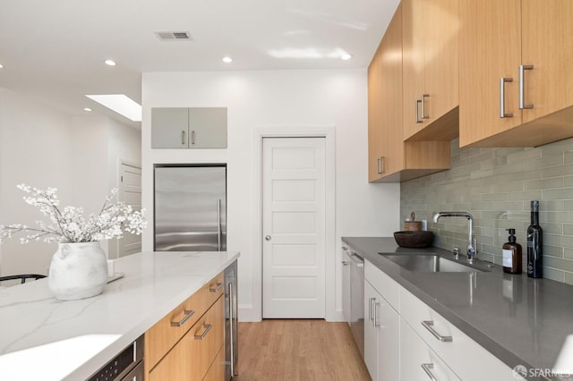 kitchen featuring sink, decorative backsplash, light stone counters, light hardwood / wood-style floors, and stainless steel appliances