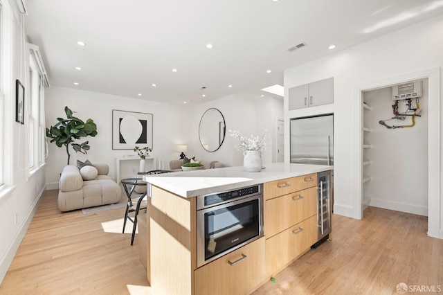 kitchen featuring stainless steel appliances, a kitchen island, light brown cabinetry, and light hardwood / wood-style flooring