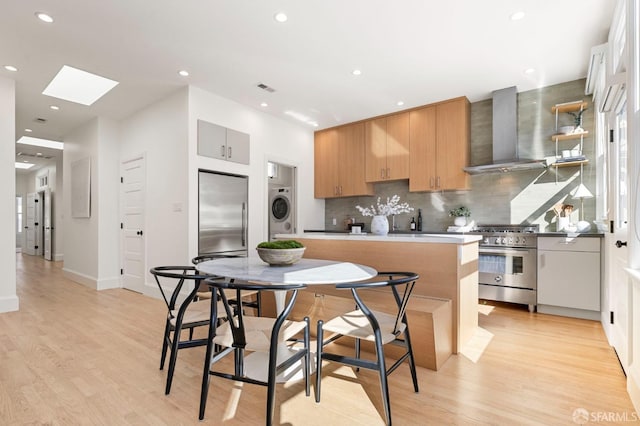 kitchen with wall chimney exhaust hood, high quality appliances, washer / clothes dryer, and light wood-type flooring