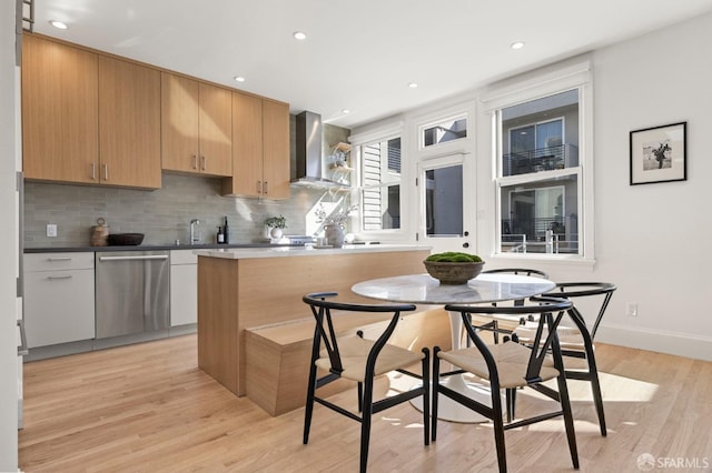 kitchen with wall chimney exhaust hood, tasteful backsplash, light wood-type flooring, stainless steel dishwasher, and white cabinets