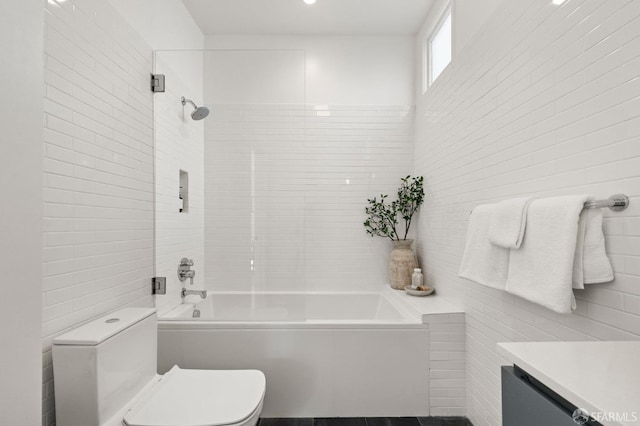 full bathroom featuring tiled shower / bath, vanity, toilet, and tile walls