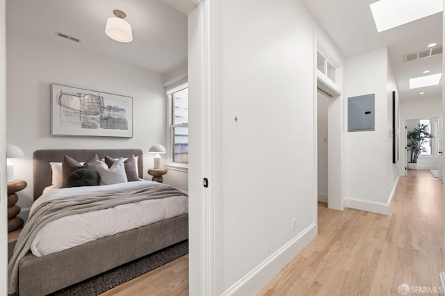 bedroom featuring electric panel, a skylight, and light hardwood / wood-style flooring