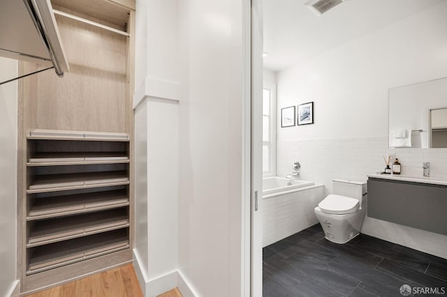 bathroom featuring tile walls, hardwood / wood-style flooring, vanity, toilet, and a bath