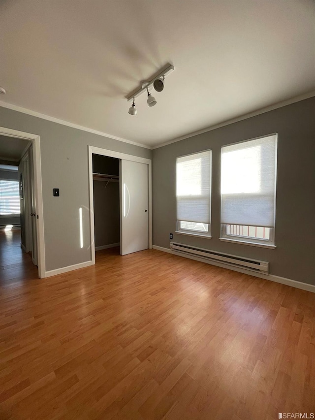 unfurnished bedroom featuring a closet, rail lighting, hardwood / wood-style flooring, and a baseboard heating unit