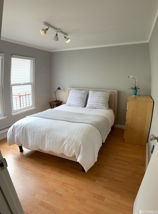 bedroom featuring crown molding, track lighting, and light hardwood / wood-style flooring