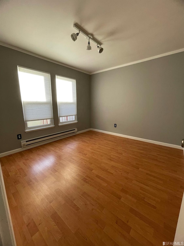 unfurnished room featuring crown molding, track lighting, a baseboard heating unit, and hardwood / wood-style floors