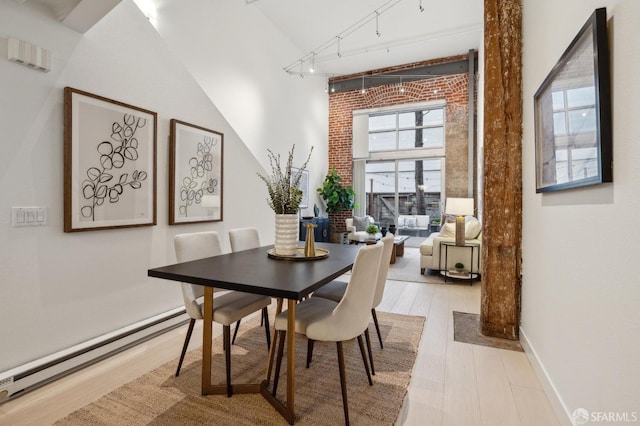 dining area with a high ceiling, light hardwood / wood-style flooring, a baseboard radiator, and plenty of natural light