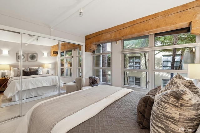 bedroom featuring track lighting, beam ceiling, and a closet