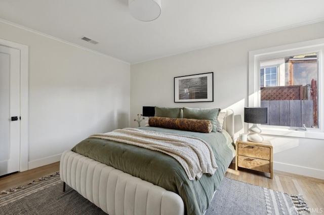 bedroom with visible vents, crown molding, baseboards, and wood finished floors