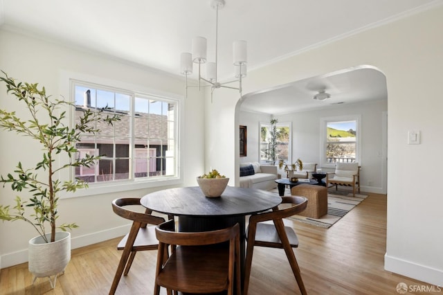 dining area featuring light wood finished floors, arched walkways, and ornamental molding