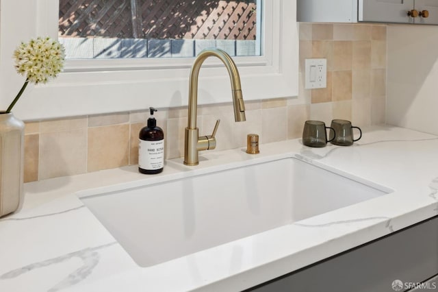 interior details with light stone counters, a sink, and backsplash