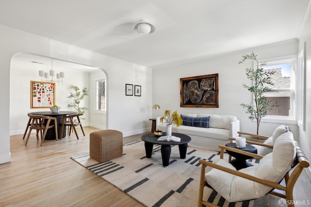 living area featuring light wood-style flooring, arched walkways, baseboards, and ornamental molding