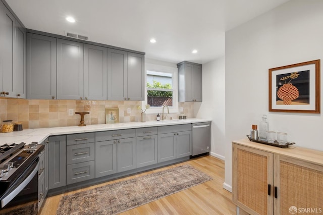 kitchen with range with gas cooktop, visible vents, gray cabinetry, stainless steel dishwasher, and a sink