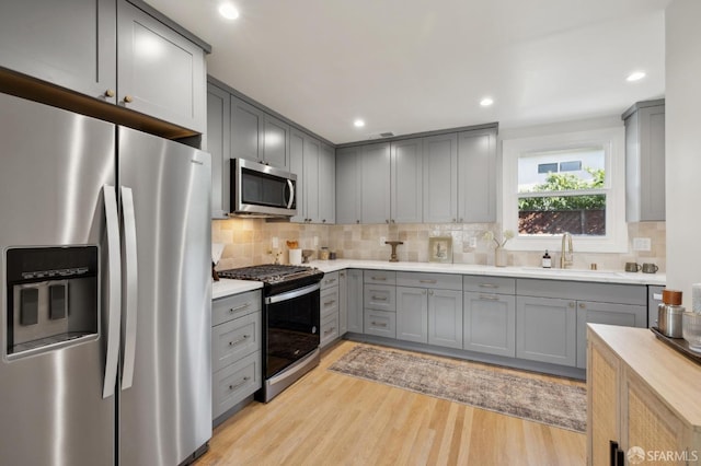 kitchen with a sink, light countertops, appliances with stainless steel finishes, gray cabinets, and light wood finished floors