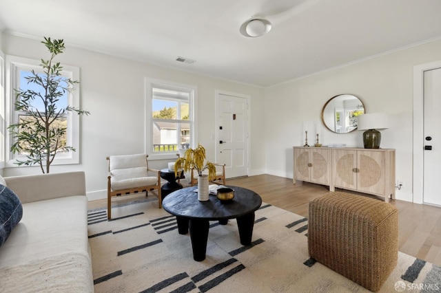 living room with baseboards, wood finished floors, visible vents, and crown molding