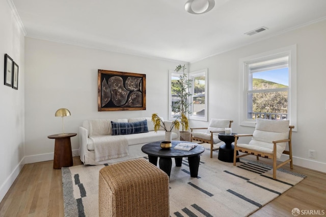 living area featuring a healthy amount of sunlight, light wood-style flooring, visible vents, and ornamental molding