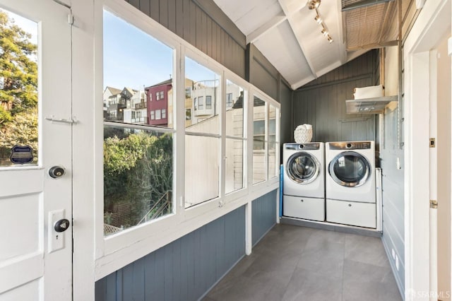 clothes washing area featuring washer and dryer, laundry area, rail lighting, and wooden walls